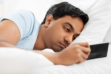 Image showing sleepy indian man with smartphone lying in bed
