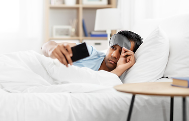 Image showing sleepy indian man with smartphone lying in bed