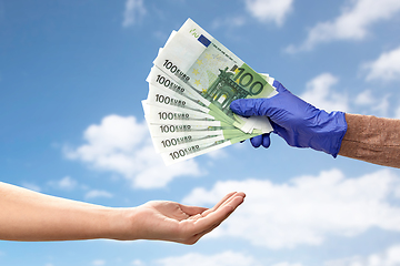 Image showing one hand in medical glove giving money to another