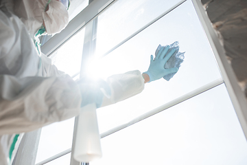 Image showing Coronavirus Pandemic. A disinfector in a protective suit and mask sprays disinfectants in the house or office