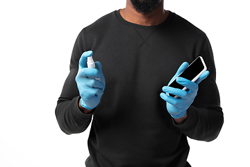 Image showing How coronavirus changed our lives. Young man disinfecting gadgets surfaces on white background