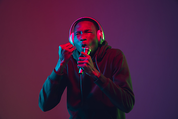 Image showing African-american man\'s portrait with headphones isolated on gradient studio background in neon light