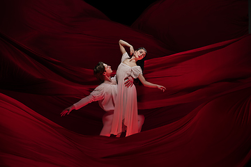 Image showing Young and graceful ballet dancers on billowing red cloth background in classic action. Art, motion, action, flexibility, inspiration concept.