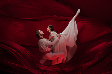 Image showing Young and graceful ballet dancers on billowing red cloth background in classic action. Art, motion, action, flexibility, inspiration concept.