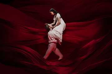 Image showing Young and graceful ballet dancers on billowing red cloth background in classic action. Art, motion, action, flexibility, inspiration concept.