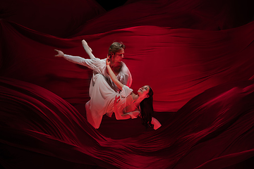 Image showing Young and graceful ballet dancers on billowing red cloth background in classic action. Art, motion, action, flexibility, inspiration concept.