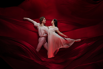 Image showing Young and graceful ballet dancers on billowing red cloth background in classic action. Art, motion, action, flexibility, inspiration concept.