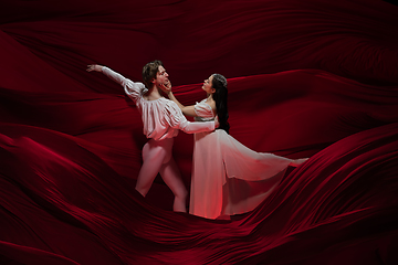 Image showing Young and graceful ballet dancers on billowing red cloth background in classic action. Art, motion, action, flexibility, inspiration concept.