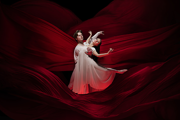 Image showing Young and graceful ballet dancers on billowing red cloth background in classic action. Art, motion, action, flexibility, inspiration concept.