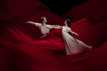 Image showing Young and graceful ballet dancers on billowing red cloth background in classic action. Art, motion, action, flexibility, inspiration concept.