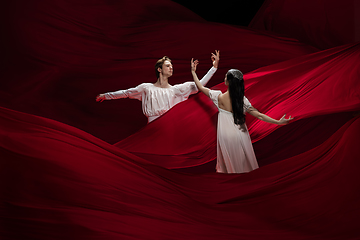 Image showing Young and graceful ballet dancers on billowing red cloth background in classic action. Art, motion, action, flexibility, inspiration concept.