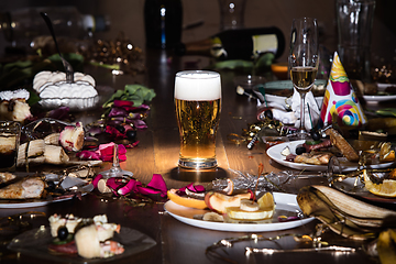 Image showing Early morning after the party. Glass of light, cold lager, beer on the table with confetti and serpentine, leftovers, flower petals