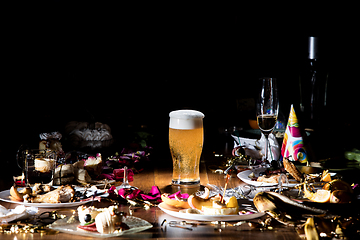 Image showing Early morning after the party. Glass of light, cold lager, beer on the table with confetti and serpentine, leftovers, flower petals