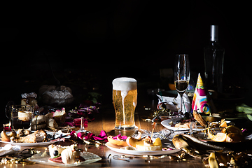 Image showing Early morning after the party. Glass of light, cold lager, beer on the table with confetti and serpentine, leftovers, flower petals