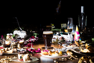 Image showing Early morning after the party. Glass of dark, cold stout, beer on the table with confetti and serpentine, leftovers, flower petals