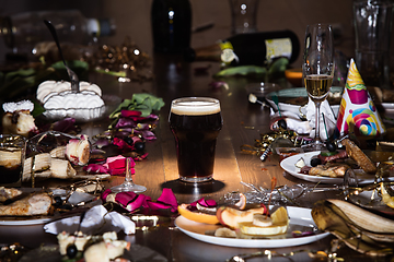 Image showing Early morning after the party. Glass of dark, cold stout, beer on the table with confetti and serpentine, leftovers, flower petals