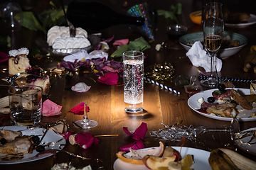 Image showing Early morning after the party. Glass of pure, cold water on the table with confetti and serpentine, leftovers, flower petals