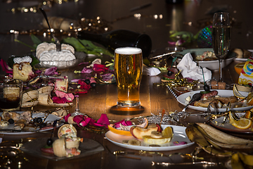 Image showing Early morning after the party. Glass of light, cold lager, beer on the table with confetti and serpentine, leftovers, flower petals