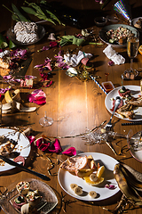Image showing Early morning after the party. Glasses and plates on the table with confetti and serpentine, leftovers, flower petals