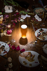 Image showing Early morning after the party. Glass of light, cold lager, beer on the table with confetti and serpentine, leftovers, flower petals