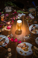 Image showing Early morning after the party. Glass of light, cold lager, beer on the table with confetti and serpentine, leftovers, flower petals