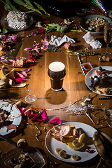 Image showing Early morning after the party. Glass of dark, cold stout, beer on the table with confetti and serpentine, leftovers, flower petals