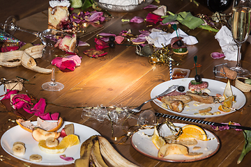 Image showing Early morning after the party. Glasses and plates on the table with confetti and serpentine, leftovers, flower petals