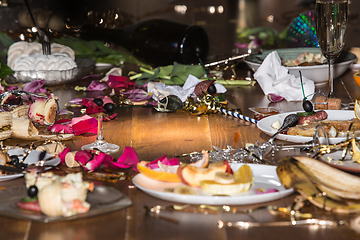 Image showing Early morning after the party. Glasses and plates on the table with confetti and serpentine, leftovers, flower petals