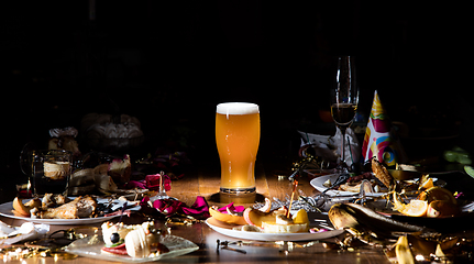 Image showing Early morning after the party. Glass of light, cold lager, beer on the table with confetti and serpentine, leftovers, flower petals