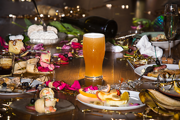 Image showing Early morning after the party. Glass of light, cold lager, beer on the table with confetti and serpentine, leftovers, flower petals