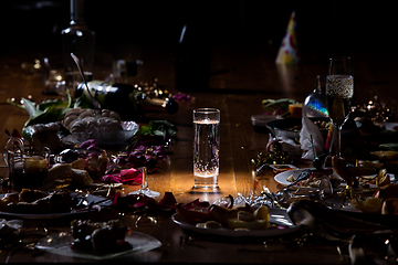 Image showing Early morning after the party. Glass of pure, cold water on the table with confetti and serpentine, leftovers, flower petals