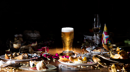 Image showing Early morning after the party. Glass of light, cold lager, beer on the table with confetti and serpentine, leftovers, flower petals