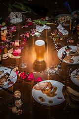 Image showing Early morning after the party. Glass of light, cold lager, beer on the table with confetti and serpentine, leftovers, flower petals