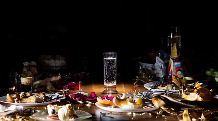 Image showing Early morning after the party. Glass of pure, cold water on the table with confetti and serpentine, leftovers, flower petals