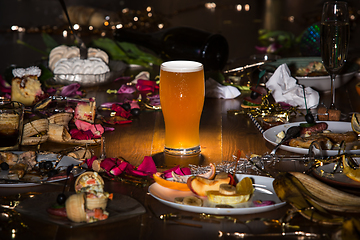 Image showing Early morning after the party. Glass of light, cold lager, beer on the table with confetti and serpentine, leftovers, flower petals