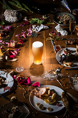 Image showing Early morning after the party. Glass of light, cold lager, beer on the table with confetti and serpentine, leftovers, flower petals