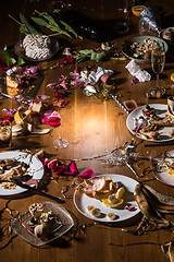 Image showing Early morning after the party. Glasses and plates on the table with confetti and serpentine, leftovers, flower petals