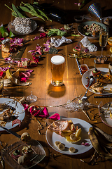 Image showing Early morning after the party. Glass of light, cold lager, beer on the table with confetti and serpentine, leftovers, flower petals