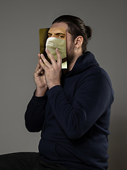 Image showing Be safe and read to become someone else - man covering face with book in face mask while reading on grey background