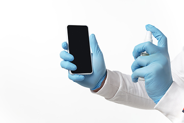 Image showing How coronavirus changed our lives. Young man disinfecting gadgets surfaces on white background