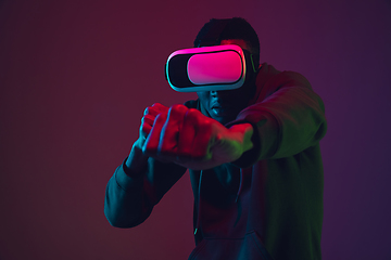 Image showing African-american man\'s portrait in VR-headset isolated on gradient studio background in neon light