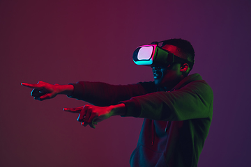Image showing African-american man\'s portrait in VR-headset isolated on gradient studio background in neon light
