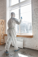 Image showing Coronavirus Pandemic. A disinfector in a protective suit and mask sprays disinfectants in the house or office