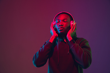 Image showing African-american man\'s portrait with headphones isolated on gradient studio background in neon light