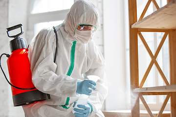 Image showing Coronavirus Pandemic. A disinfector in a protective suit and mask sprays disinfectants in the house or office