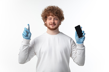 Image showing How coronavirus changed our lives. Young man disinfecting gadgets surfaces on white background