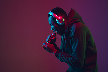 Image showing African-american man\'s portrait with headphones isolated on gradient studio background in neon light