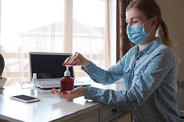 Image showing Young woman in face mask disinfecting gadgets surfaces on her workplace