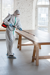 Image showing Coronavirus Pandemic. A disinfector in a protective suit and mask sprays disinfectants in the house or office