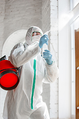 Image showing Coronavirus Pandemic. A disinfector in a protective suit and mask sprays disinfectants in the house or office